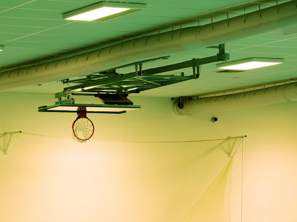 Techo de aro de baloncesto plegado abajo. La cesta con red blanca en interior gimnasio deporte metal techo fondo - Foto, Imagen
