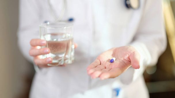 Woman doctor offers to take pill for cure illness. Nurse is holding one medical capsule and glass of water. - Photo, Image