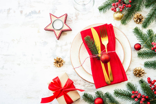 Comida navideña, mesa de Navidad con plato blanco, cubiertos dorados y decoraciones navideñas sobre fondo de madera claro. Vista superior. - Foto, imagen