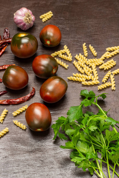 Brown tomatoes, parsley sprigs, spices, and pasta. Top view.  - Foto, afbeelding