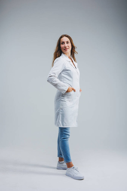moderno médico alegre en una bata blanca sobre un fondo gris. Médico mujer con una sonrisa en la cara - Foto, imagen