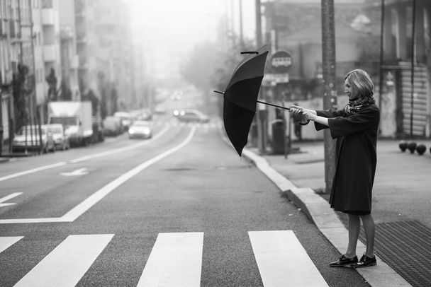 Kobieta otwiera parasol, przechodząc przez ulicę we mgle. Czarno-białe zdjęcie. - Zdjęcie, obraz