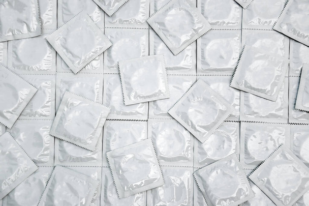Many white packages of unopened condoms as a background. Using a condom to reduce the chance of pregnancy or sexually transmitted diseases, STDs. The concept of safe sex and reproductive health. - Photo, image