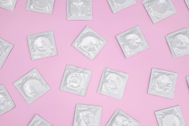 Many white packages of unopened condoms on a pink background. Using a condom to reduce the chance of pregnancy or sexually transmitted diseases, STDs. The concept of safe sex and reproductive health. - Photo, image