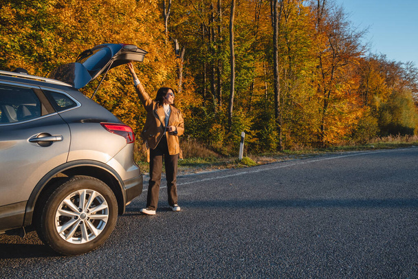 On forest background, smiling woman closes trunk of parked car. copy space - Photo, Image
