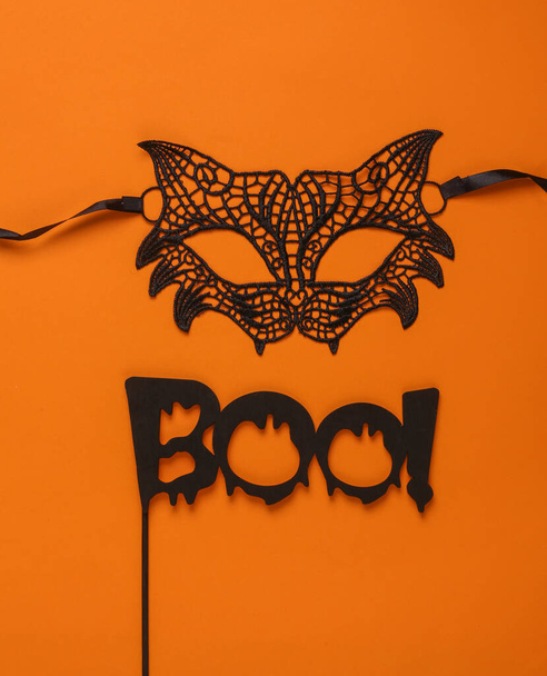 Karnawał koronkowa maska kota i słowo boo na patyku, pomarańczowe tło. Halloween party. Widok z góry - Zdjęcie, obraz
