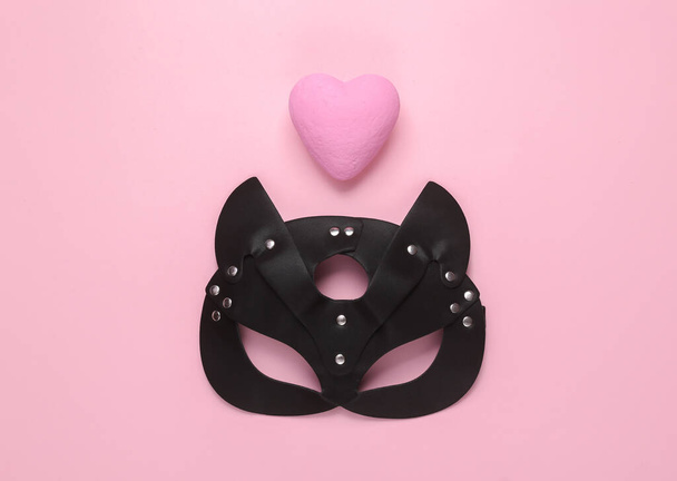 Leather bdsm cat mask and heart on pink background. Sexual role playing. Love concept. Top view. Flat lay - Photo, Image