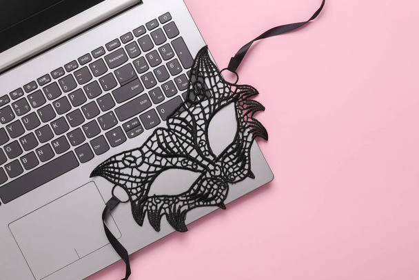 Online erotyczny czat. Maska koronkowa z laptopem na różowym tle. Widok góry. układanie płaskie - Zdjęcie, obraz