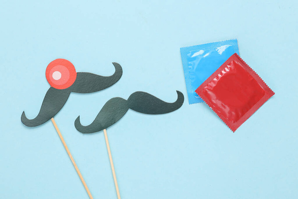 Поняття одностатевих стосунків. презервативи і дві пари вусів на паличках на синьому фоні
 - Фото, зображення