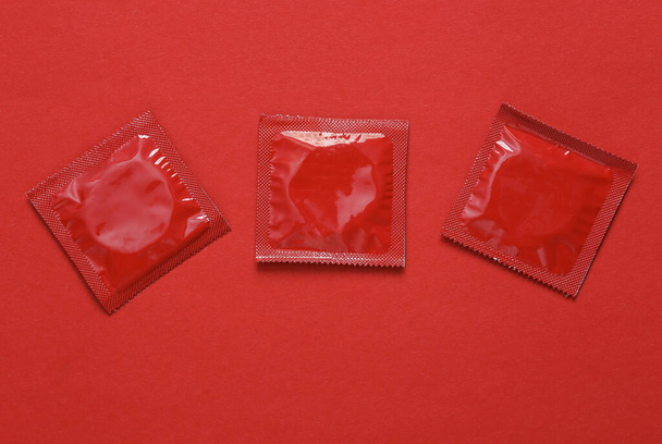 Kolme punaista kondomipakkausta punaisella taustalla. Yläkuva - Valokuva, kuva