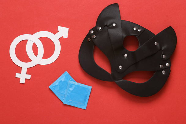 Skórzana maska kota BDSM z opakowaniami prezerwatyw i symboli płci na czerwonym tle. Role play gry seksualne - Zdjęcie, obraz