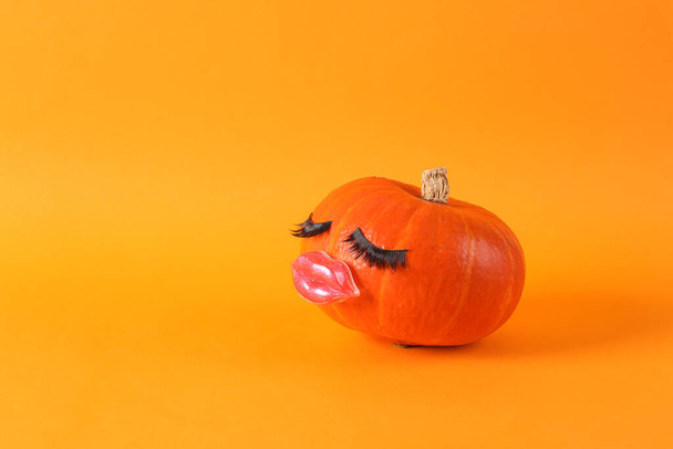 Kürbis mit falschen Wimpern und Lippen auf orangefarbenem Hintergrund. Kleine Schönheit, Halloween-Konzept. Kreative Gestaltung - Foto, Bild