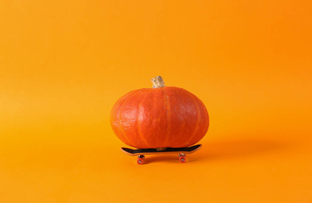 Creative idea, minimal still life. Pumpkin on a skateboard, orange background - Foto, imagen