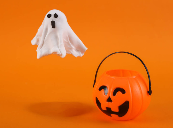 Fantasma de plasticina feito à mão com balde de doces de abóbora no fundo laranja. Conceito de Halloween. Truques ou travessuras - Foto, Imagem