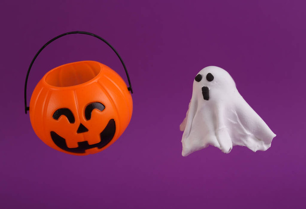 Handgemachtes Knetgummi-Gespenst mit Kürbis-Jack-Bonbon-Eimer auf lila Hintergrund. Halloween-Konzept. Süßes oder Saures - Foto, Bild