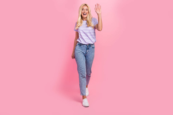 Full length portrait of cheerful lovely person toothy smile arm palm waving walking isolated on pink color background. - 写真・画像
