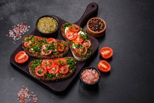 Tasty bruschetta with tomatoes, mozzarella, basil, spices and herbs on a dark concrete background - Foto, imagen