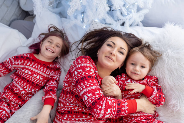 People in same family look pajamas, kidding at home christmas day. New Year holidays. Happy funny child boy son, daughter, girl with mother spend time together, enjoying, fool around in bed in bedroom - Zdjęcie, obraz