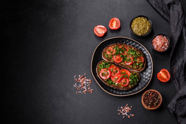 Leckere Bruschetta mit Tomaten, Mozzarella, Basilikum, Gewürzen und Kräutern auf dunklem Betongrund - Foto, Bild