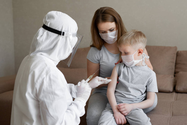 Doctor in personal protective suit or PPE inject vaccine shot to stimulating immunity of a boy at risk of coronavirus infection. Coronavirus,covid-19 and vaccination concept. - Foto, Bild