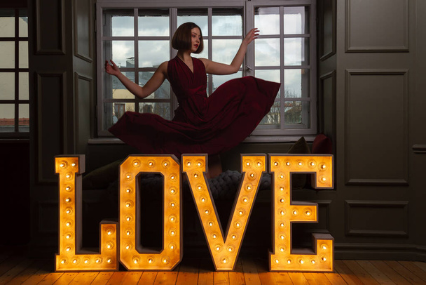 Жінка з руками в повітрі в червоній сукні, що падає за словом Любов, зроблена з сяючих літер
 - Фото, зображення
