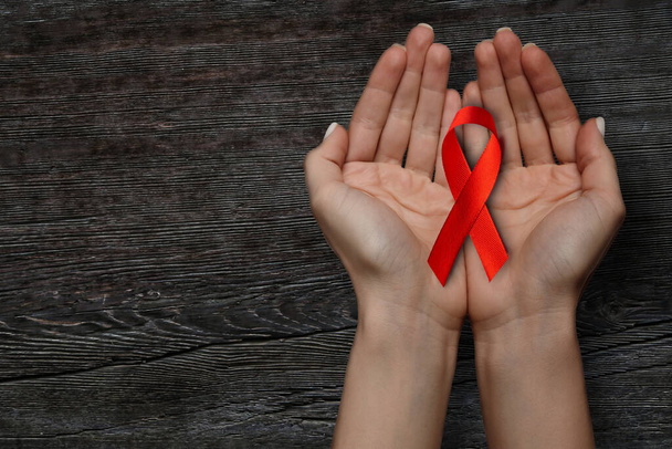 a red ribbon for the WORLD AIDS symbol is held on a wooden table - Φωτογραφία, εικόνα