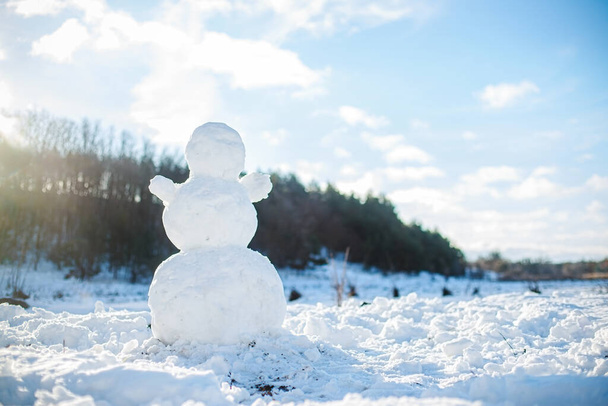 φωτογραφία του χιονιού στο οποίο στέκεται μεγάλο χιονάνθρωπο. φιγούρα του χιονάνθρωπου στο φόντο του δάσους φωτίζεται από τον ήλιο. Ηλιόλουστη μέρα το χειμώνα. Λαμπρό χιόνι μετά από έντονη χιονόπτωση. - Φωτογραφία, εικόνα