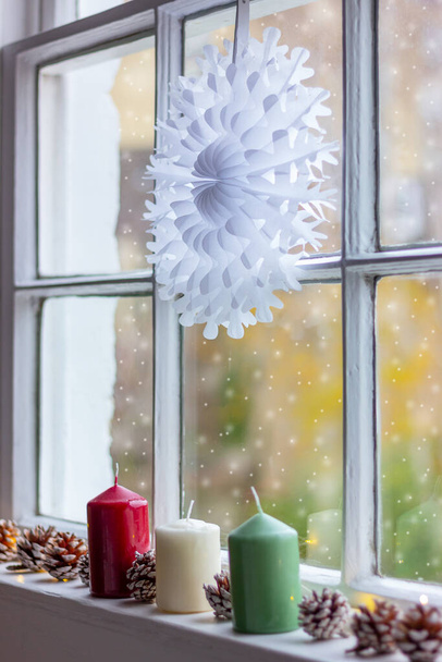 nagy papír fehér hópehely, gyertyák és kúpok az ablakon. tél, újév és karácsonyi dekorációk - Fotó, kép