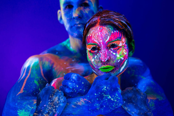 Portrait of a beefy man and woman painted in ultraviolet powder. Body art glowing in ultraviolet light - Foto, imagen