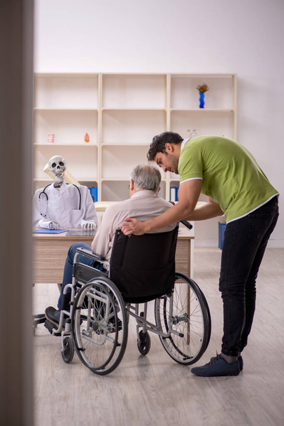 Ηλικιωμένος άνδρας ασθενής σε αναπηρική καρέκλα επισκέπτεται σκελετό γιατρό - Φωτογραφία, εικόνα