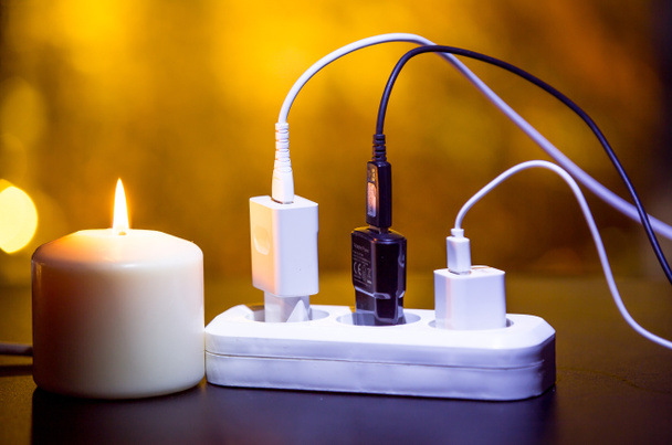 Blackout-Konzept. elektrisches Ladegerät mit Kabel in der Nähe der brennenden Kerze auf dunklem Hintergrund. - Foto, Bild