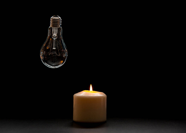 Горить свічка біля вимкненої лампочки в темному будинку. Відключення електроенергії, втрата навантаження, криза енергії або відключення електроенергії, концепт-зображення
. - Фото, зображення