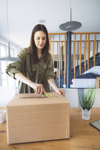 Young caucasian woman receiving a big box of her online orders. Woman opening the package, getting excited to see the stuff she bought. High quality photo - Foto, Imagen