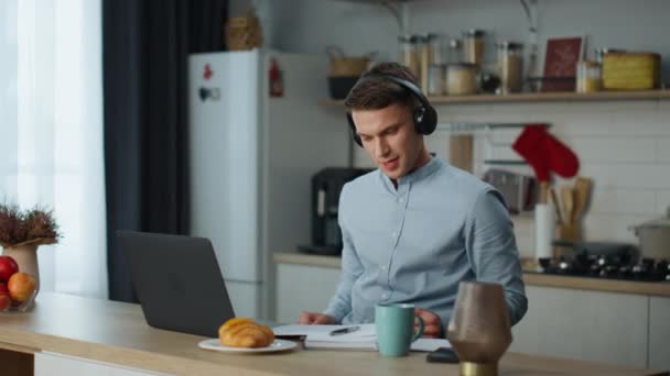 Χαλαρός ευτυχισμένος άνθρωπος ακούγοντας μουσική με ακουστικά που αναζητούν πληροφορίες σχετικά με το laptop χρησιμοποιώντας το διαδίκτυο στο σπίτι κουζίνα. Ελκυστικός νεαρός που χορεύει με μελωδία από ασύρματα ακουστικά. Ελεύθερη κυκλοφορία των εργαζομένων. - Πλάνα, βίντεο