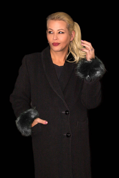 Mulher loira atraente vestindo um casaco de caxemira preto em um fundo preto - Foto, Imagem