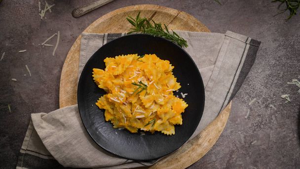 Farfalle pasta with pumpkin sauce in a ceramic plate on a dark stone kitchen counter top. - Photo, Image