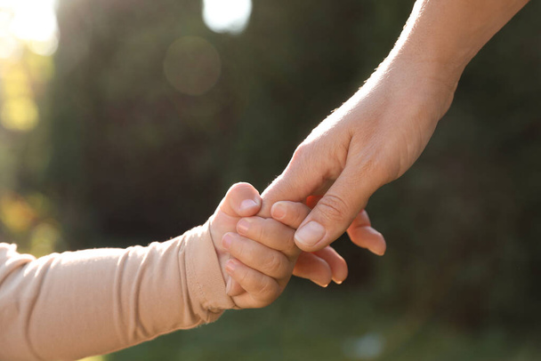 Daughter holding mother's hand outdoors, closeup view - Foto, Imagen