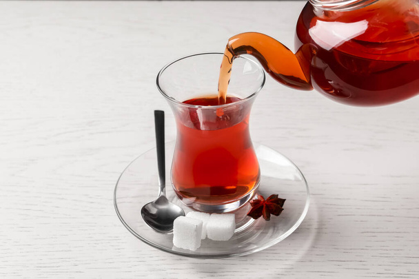 Pouring traditional Turkish tea from pot into glass on white wooden table - Фото, зображення