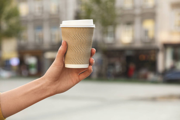Woman holding paper takeaway cup on city street, closeup with space for text. Coffee to go - Zdjęcie, obraz