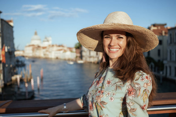 Portrait of happy elegant woman in floral dress with hat sightseeing on Accademia bridge in Venice, Italy. - Fotó, kép
