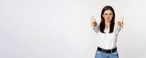 Disappointed adult corporate woman showing thubms down, dislike gesture, negative feedback, complaining and grimacing, white background. - Foto, afbeelding