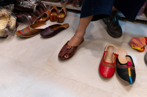 Piękna Hinduska kobieta próbuje swoich stóp do montażu kolorowych butów damskich Rajsathani w sklepie obuwniczym w słynnym Sardar Market i Ghanta ghar Wieża zegarowa w Jodhpur, Rajasthan, Indie. - Zdjęcie, obraz
