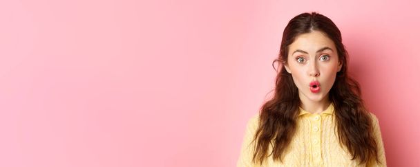 Close up portrait of surprised brunette girl saying wow, folding lips and stare amazed at camera, checking out awesome news, standing against pink background. - Photo, Image