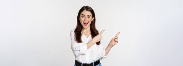 Portrait of enthusiastic smiling woman, female entrepreneur pointing fingers left and showing advertisement, showing announcement, white background. - Foto, Imagem