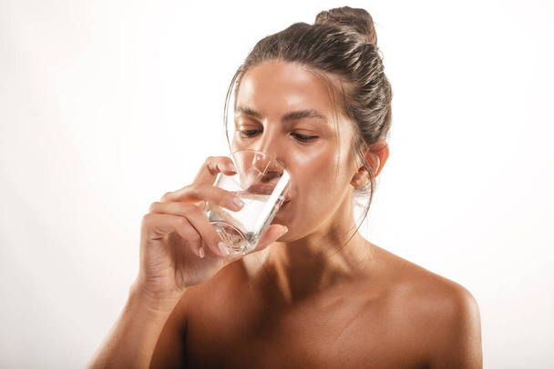 Nahaufnahme eines schönen Mädchens mit einem Brötchen, das Wasser im Studio auf weißem Hintergrund trinkt - Foto, Bild
