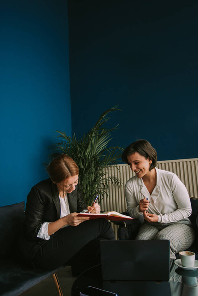 Крупным планом две деловые девушки сидят в кафе и улыбаются там, где одна из них пишет заметки - Фото, изображение