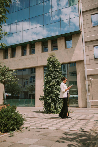Mulher de negócios bonita andando no meio dos edifícios da cidade com seu tablet - Foto, Imagem