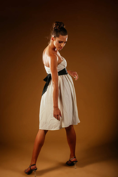 A lovely girl looking back down. She has a make up on her face and wears white dress with black belt - 写真・画像