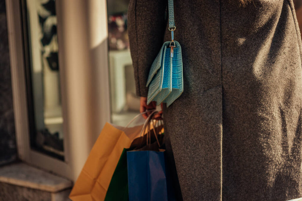 A close up photo of a girl in gray coat wearing handbag and shopping bags in her hand - Fotó, kép