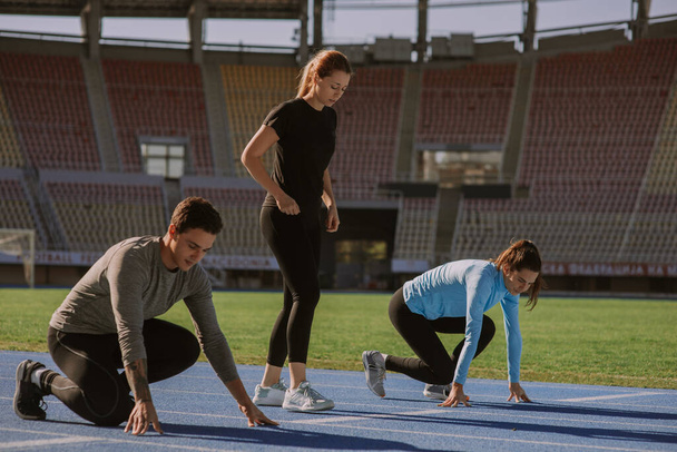 Two gorgeous girls and one handsome boy are preparing for jogging. They are exercising at the stadium, on  beautiful sunny morning - Photo, Image